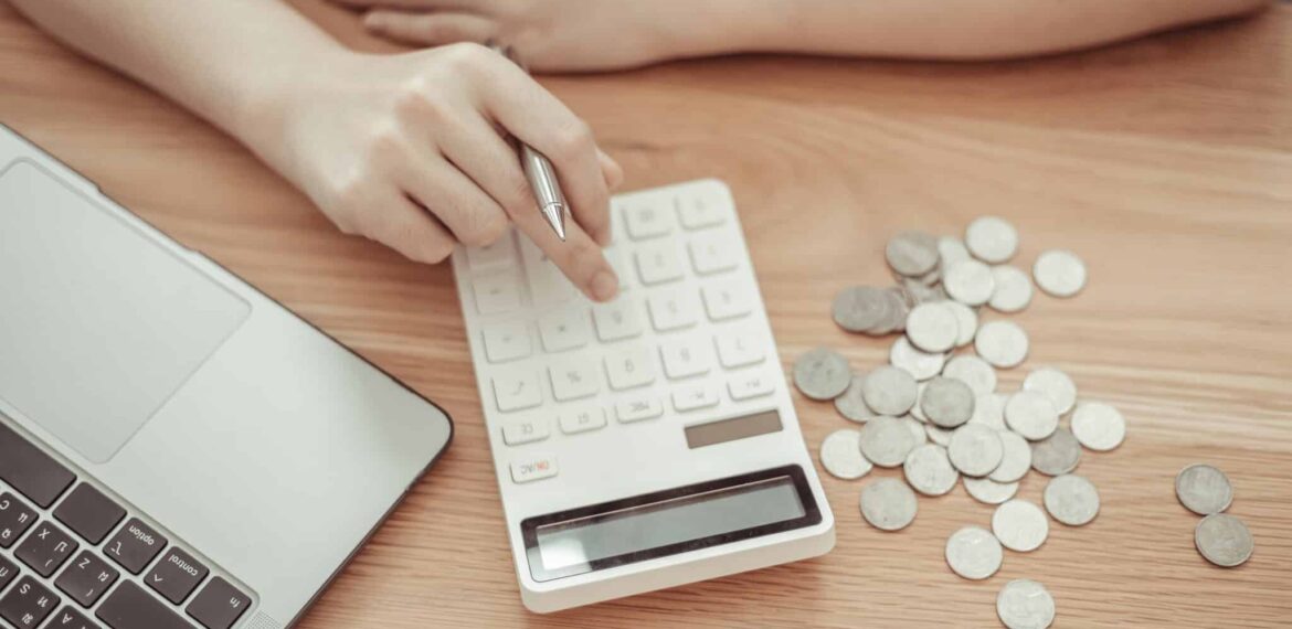 person using a calculator next to pile of coins on desktop